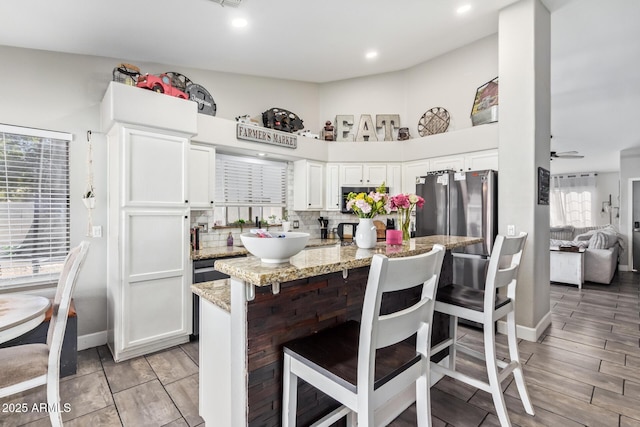 kitchen featuring white cabinetry, backsplash, a kitchen bar, ceiling fan, and light stone countertops