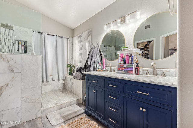 bathroom featuring vanity, vaulted ceiling, and a tile shower