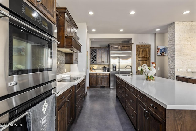 kitchen with appliances with stainless steel finishes, sink, backsplash, a kitchen island with sink, and dark brown cabinetry