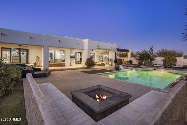 pool at dusk featuring a patio area, ceiling fan, and a fire pit