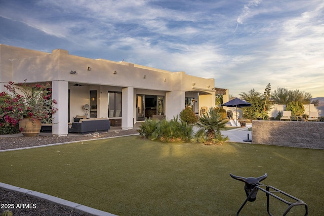 back house at dusk with an outdoor hangout area, a patio area, and a lawn