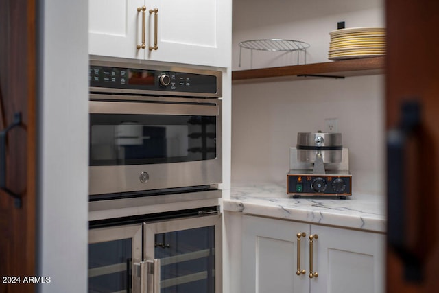 kitchen featuring wine cooler, stainless steel double oven, light stone counters, and white cabinets