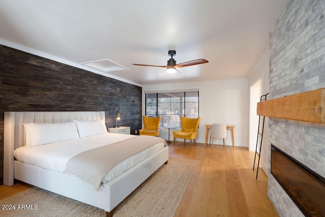 bedroom with light hardwood / wood-style floors, ceiling fan, a large fireplace, and crown molding