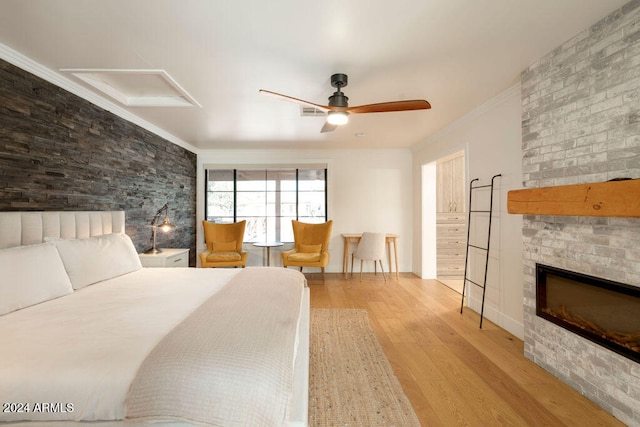 bedroom featuring a large fireplace, ceiling fan, light hardwood / wood-style flooring, and ornamental molding