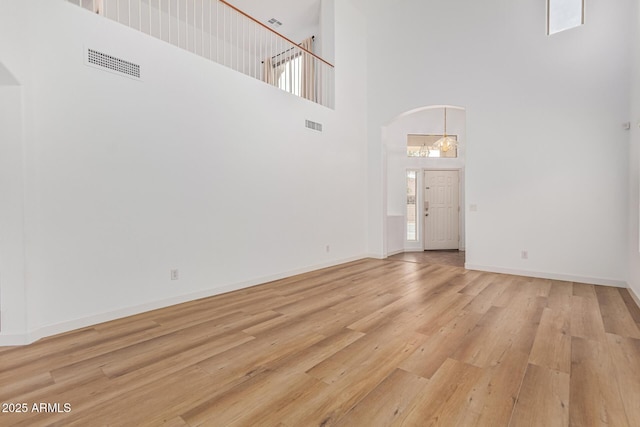 unfurnished living room with light hardwood / wood-style floors and a towering ceiling