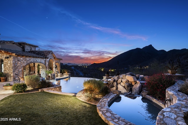 pool at dusk featuring a mountain view and a yard