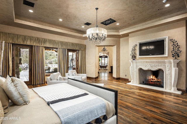 bedroom featuring access to outside, a premium fireplace, a tray ceiling, wood-type flooring, and a chandelier