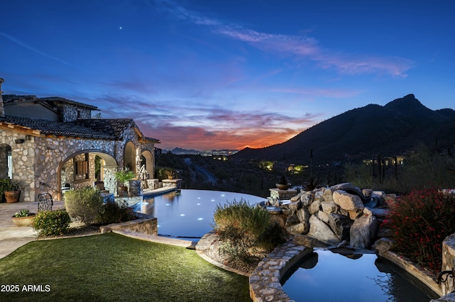 pool at dusk featuring a mountain view and a yard