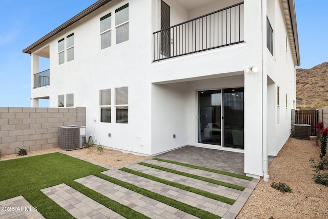 rear view of house featuring a patio, a balcony, a lawn, and central AC