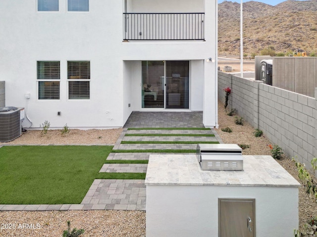 back of house featuring an outdoor kitchen, central AC unit, a mountain view, a lawn, and a balcony