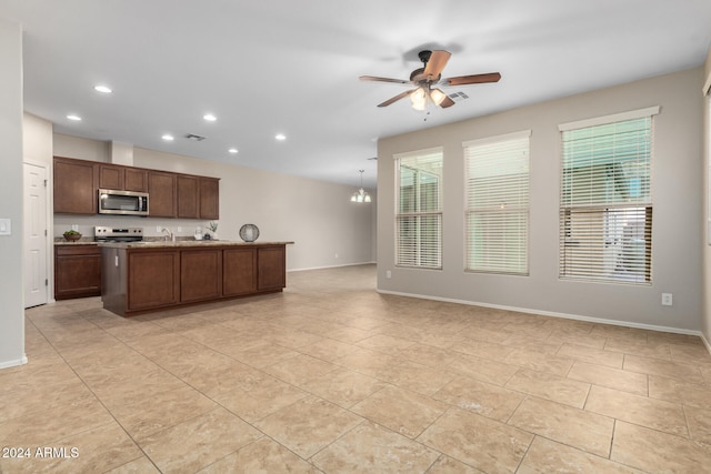 kitchen featuring ceiling fan with notable chandelier, white range with electric stovetop, a kitchen island with sink, sink, and decorative light fixtures