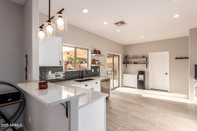 kitchen featuring pendant lighting, stainless steel dishwasher, a kitchen bar, sink, and white cabinets