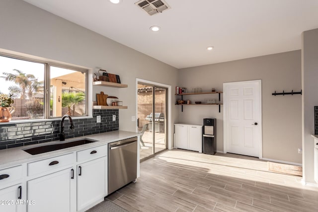 kitchen with decorative backsplash, white cabinets, stainless steel dishwasher, and sink