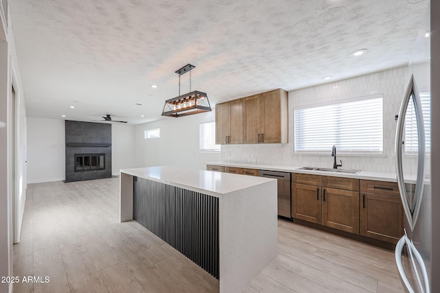 kitchen with pendant lighting, a tile fireplace, sink, appliances with stainless steel finishes, and a kitchen island