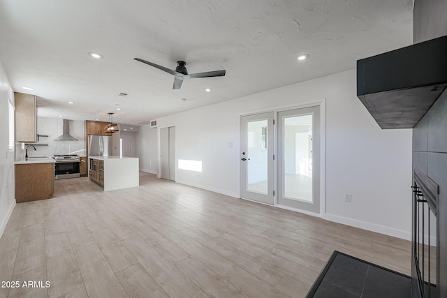 unfurnished living room with ceiling fan, a large fireplace, light wood-type flooring, and sink