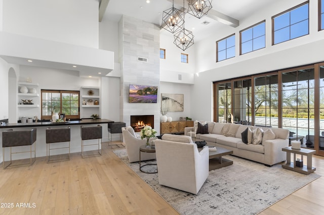 living area featuring visible vents, a tile fireplace, light wood-style flooring, beamed ceiling, and an inviting chandelier