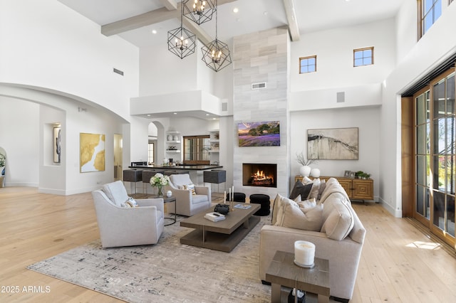 living area with arched walkways, light wood-type flooring, a tiled fireplace, and beam ceiling