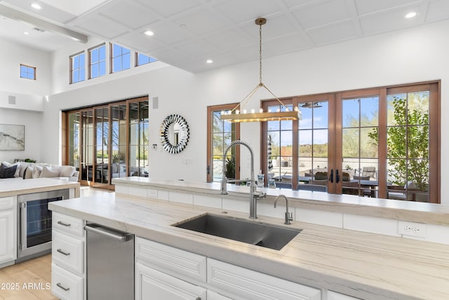 kitchen with beverage cooler, a sink, white cabinets, open floor plan, and decorative light fixtures