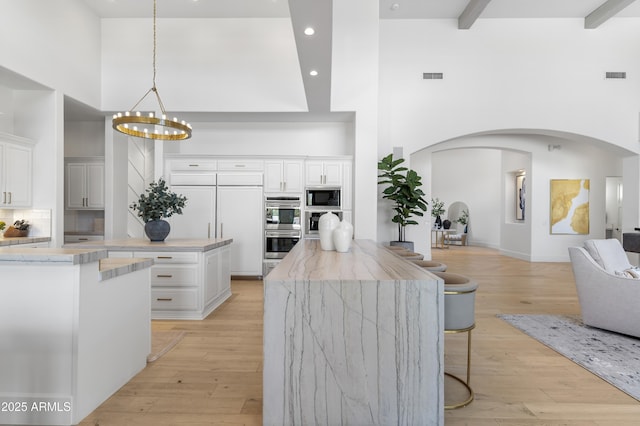 kitchen with arched walkways, pendant lighting, visible vents, white cabinetry, and built in appliances