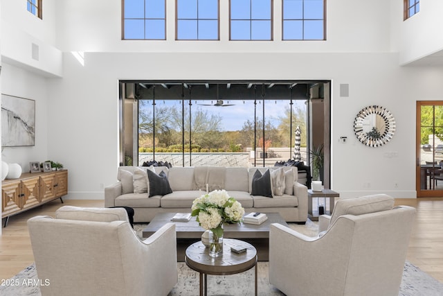 living area with a towering ceiling, light wood-style flooring, visible vents, and baseboards