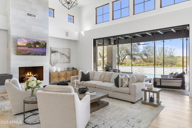 living area featuring light wood-type flooring, visible vents, a fireplace, and a high ceiling