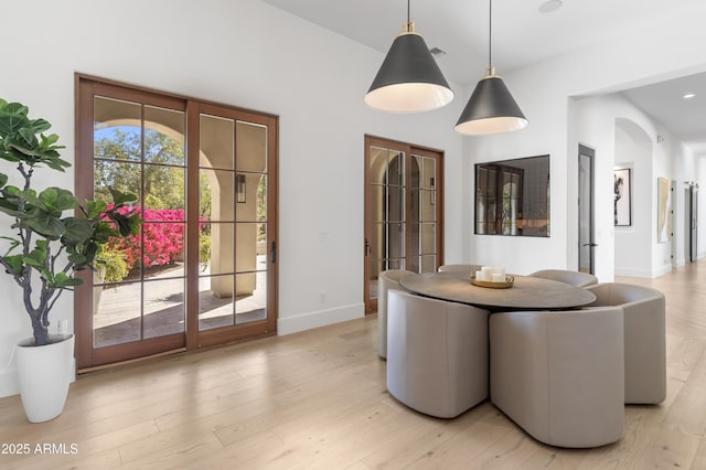 dining space with light wood-style floors, baseboards, and arched walkways