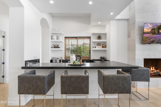 kitchen with a peninsula, light wood-type flooring, a kitchen bar, and open shelves