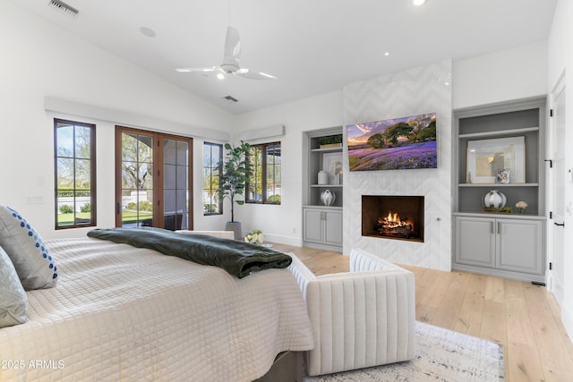 bedroom featuring french doors, lofted ceiling, visible vents, a premium fireplace, and light wood-type flooring