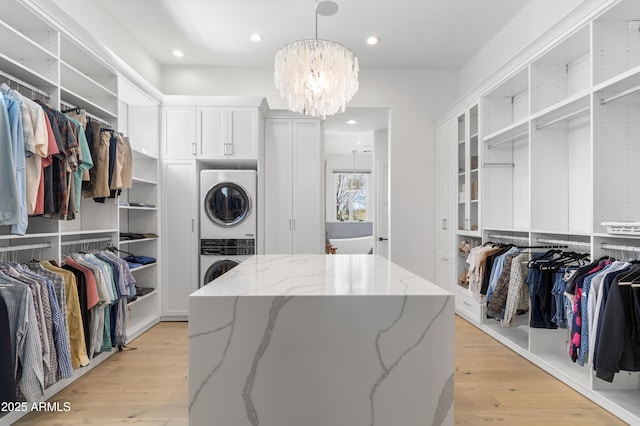 walk in closet featuring light wood-style flooring, stacked washer and clothes dryer, and an inviting chandelier