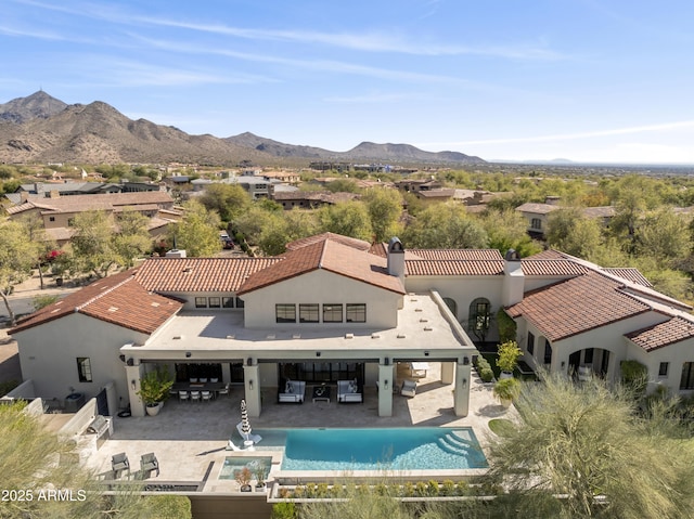 rear view of property with stucco siding, a chimney, a mountain view, and a patio