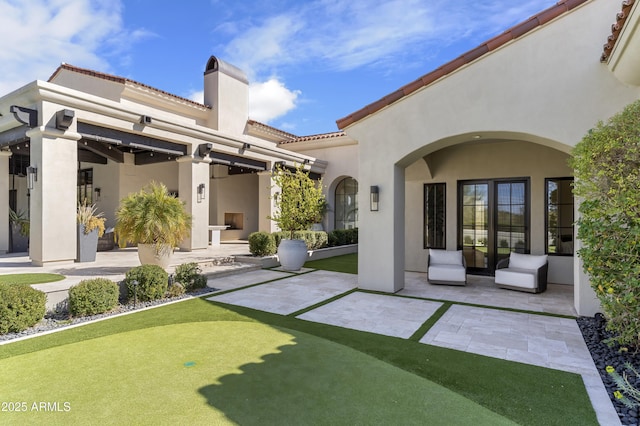 rear view of property featuring a chimney, a patio area, a tile roof, and stucco siding