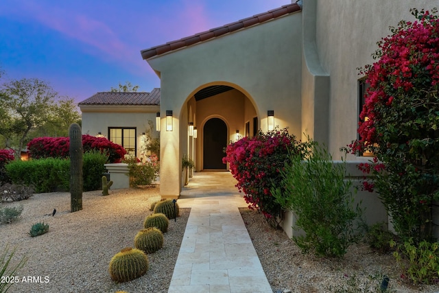 view of exterior entry with a tile roof and stucco siding