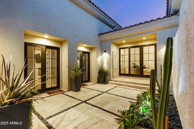 exterior entry at dusk with stucco siding, a tile roof, a patio area, and french doors