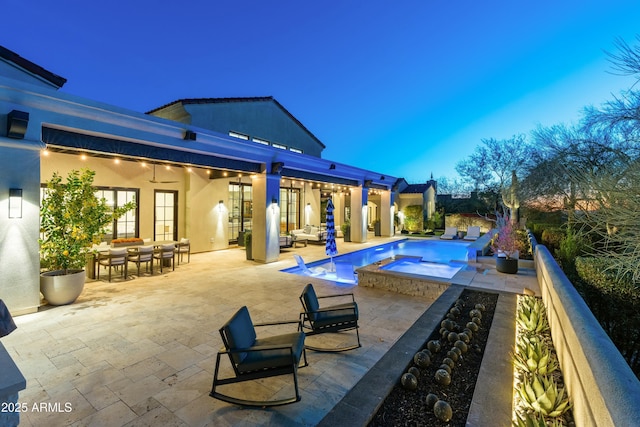 pool at dusk featuring ceiling fan, a patio, and a pool with connected hot tub