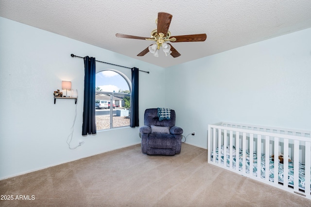 bedroom featuring a nursery area, light carpet, a textured ceiling, and ceiling fan