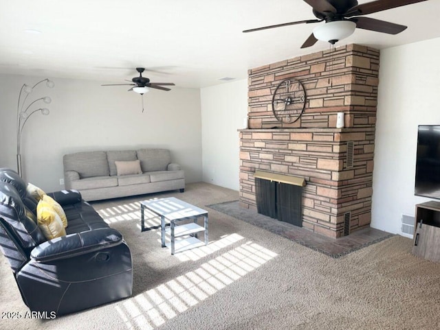 carpeted living room featuring a stone fireplace and ceiling fan