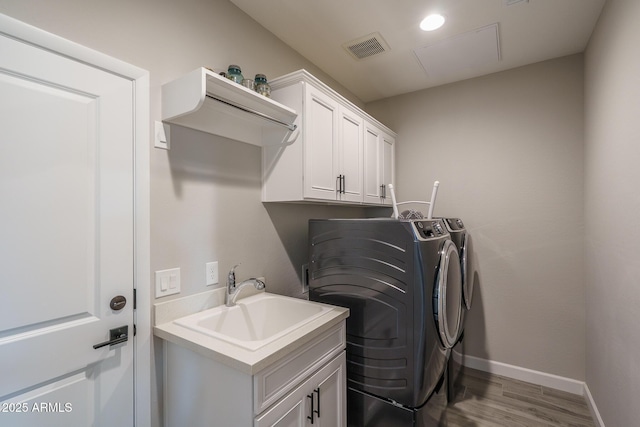 washroom featuring cabinet space, visible vents, a sink, separate washer and dryer, and wood finished floors