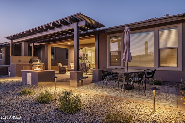 patio terrace at dusk with a grill, a fire pit, an outdoor kitchen, and outdoor dining space