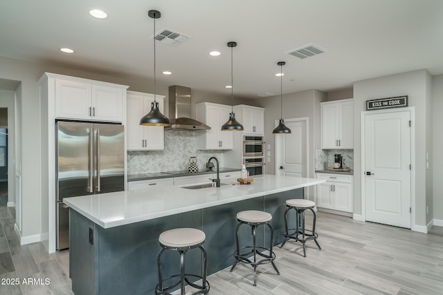 kitchen featuring visible vents, wall chimney range hood, decorative light fixtures, and white cabinetry