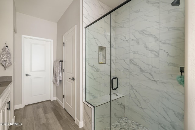 bathroom with wood finished floors, a marble finish shower, and baseboards