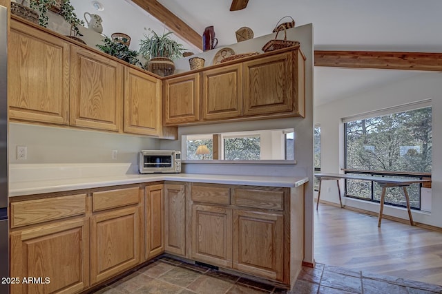 kitchen with vaulted ceiling with beams, a toaster, baseboards, light countertops, and stone finish flooring