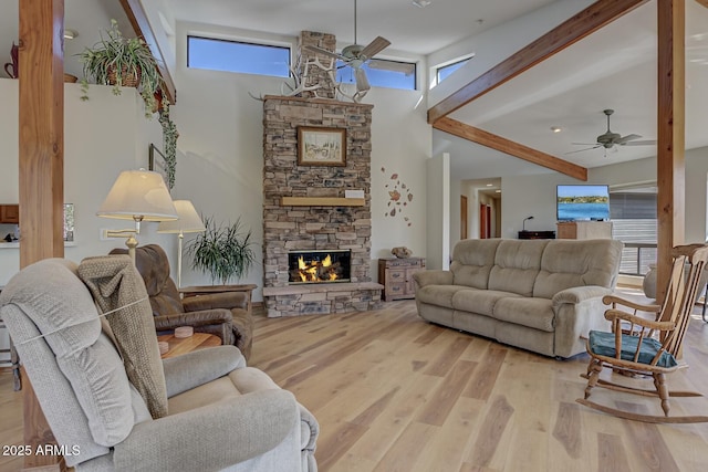 living area featuring a ceiling fan, beamed ceiling, wood finished floors, and a stone fireplace