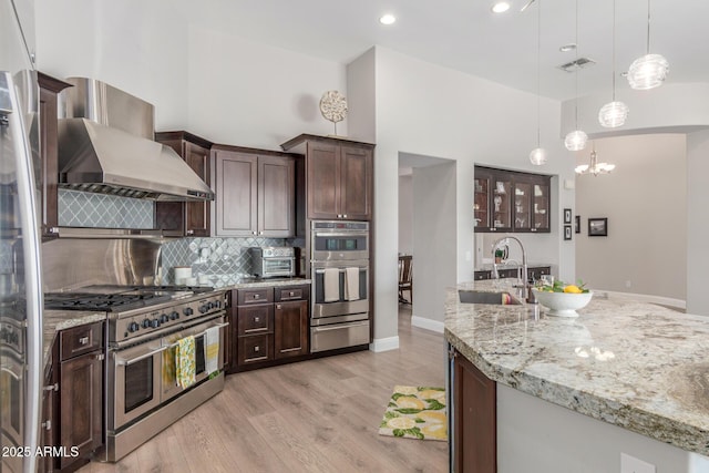 8725 E Menlo Cir, Mesa, AZ 85207 - kitchen with appliances with stainless steel finishes, wall chimney range hood, a warming drawer, dark brown cabinets, and decorative backsplash