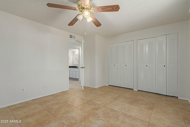 unfurnished bedroom featuring light tile patterned floors, a textured ceiling, visible vents, and multiple closets