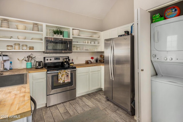 kitchen with wood counters, appliances with stainless steel finishes, white cabinetry, and stacked washer and clothes dryer