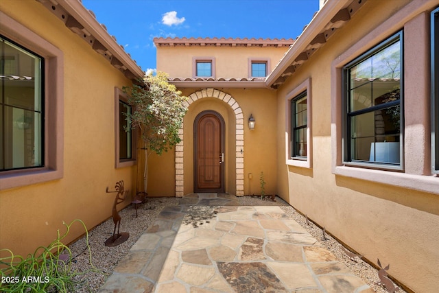 property entrance with a tiled roof, a patio, and stucco siding