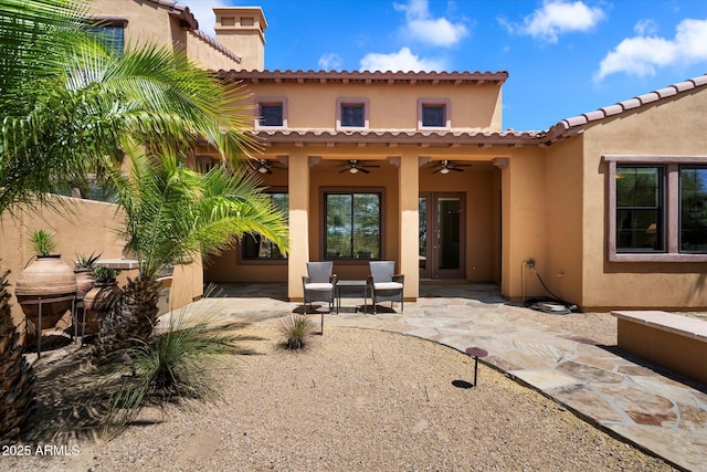 rear view of property featuring a tiled roof, a chimney, a ceiling fan, a patio area, and stucco siding