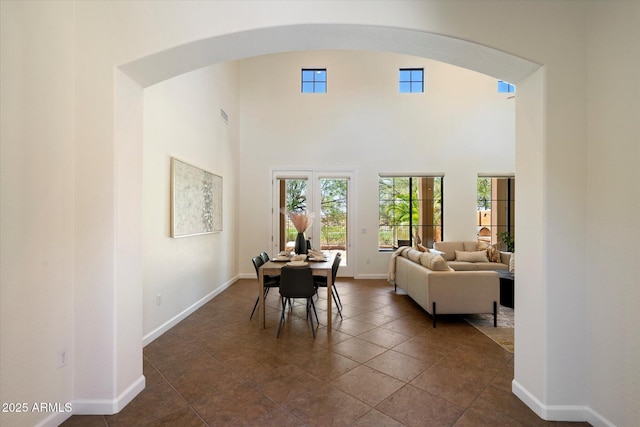 dining room featuring arched walkways, baseboards, and a towering ceiling