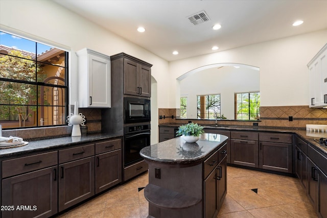 kitchen with visible vents, dark brown cabinets, dark stone countertops, backsplash, and black appliances