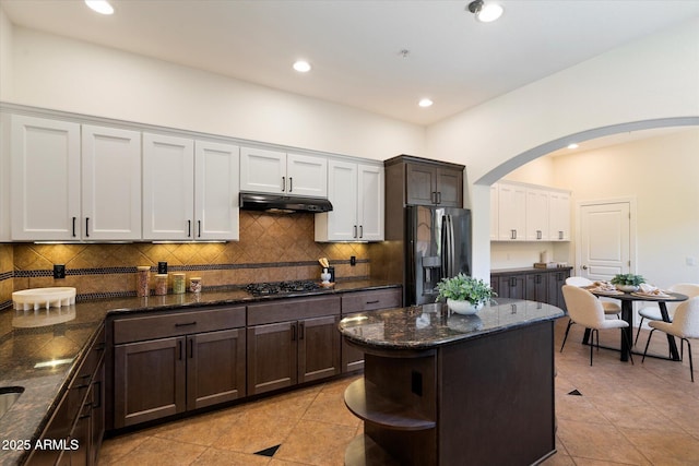 kitchen with backsplash, arched walkways, gas stovetop, black fridge, and under cabinet range hood